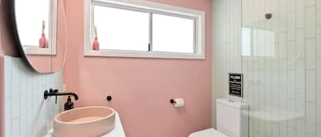 A bathroom with a pink wall, a white sink, a toilet, and a window.