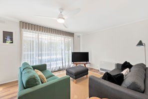 Ein Wohnzimmer mit Deckenventilator, Flachbildfernseher und zwei Sofas.
