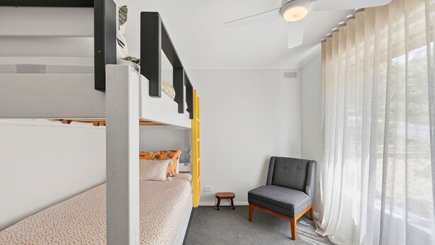 Ein Schlafraum mit Etagenbetten, Deckenventilator, kleinem Tisch, Stuhl und einem Fenster mit Vorhängen.