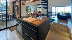 Una cocina moderna con una isla central, un comedor con muebles de madera, una escalera y una sala de estar con un sofá azul.
