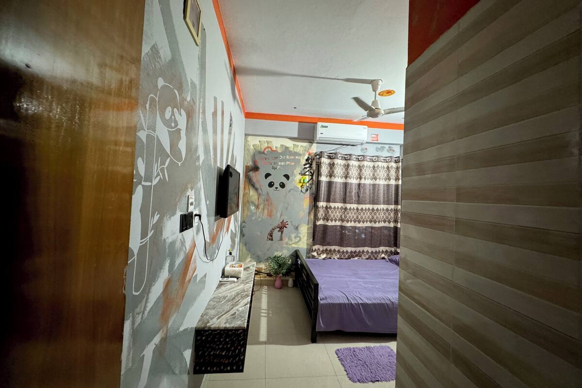 Ein Schlafzimmer mit einem Bett, einem Deckenventilator, einer Klimaanlage, einer Wand mit Wandgemälde einer Panda und einem Fenster mit Vorhang.