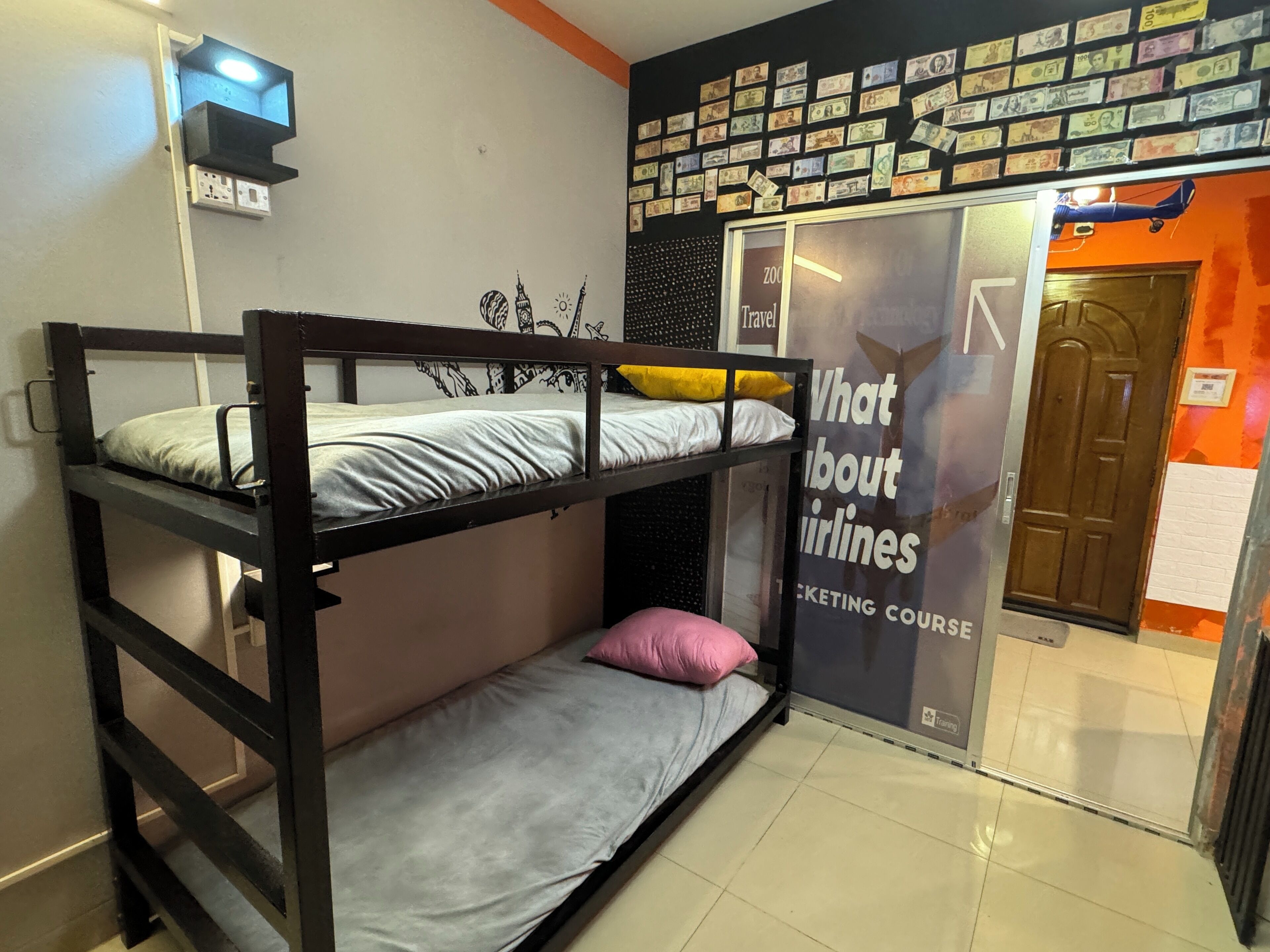 A bunk bed room with a wall decorated with currency notes, a sign about airlines, and a door to a room with orange walls.