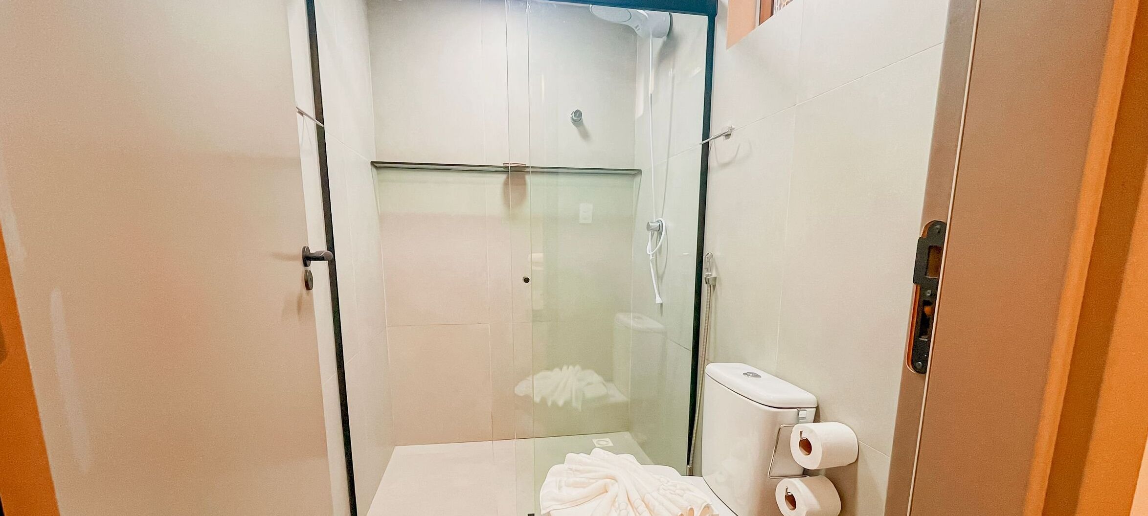 Une salle de bain moderne dotée d’une douche à parois de verre, de toilettes avec un distributeur de serviettes en papier et d’un porte-serviettes.