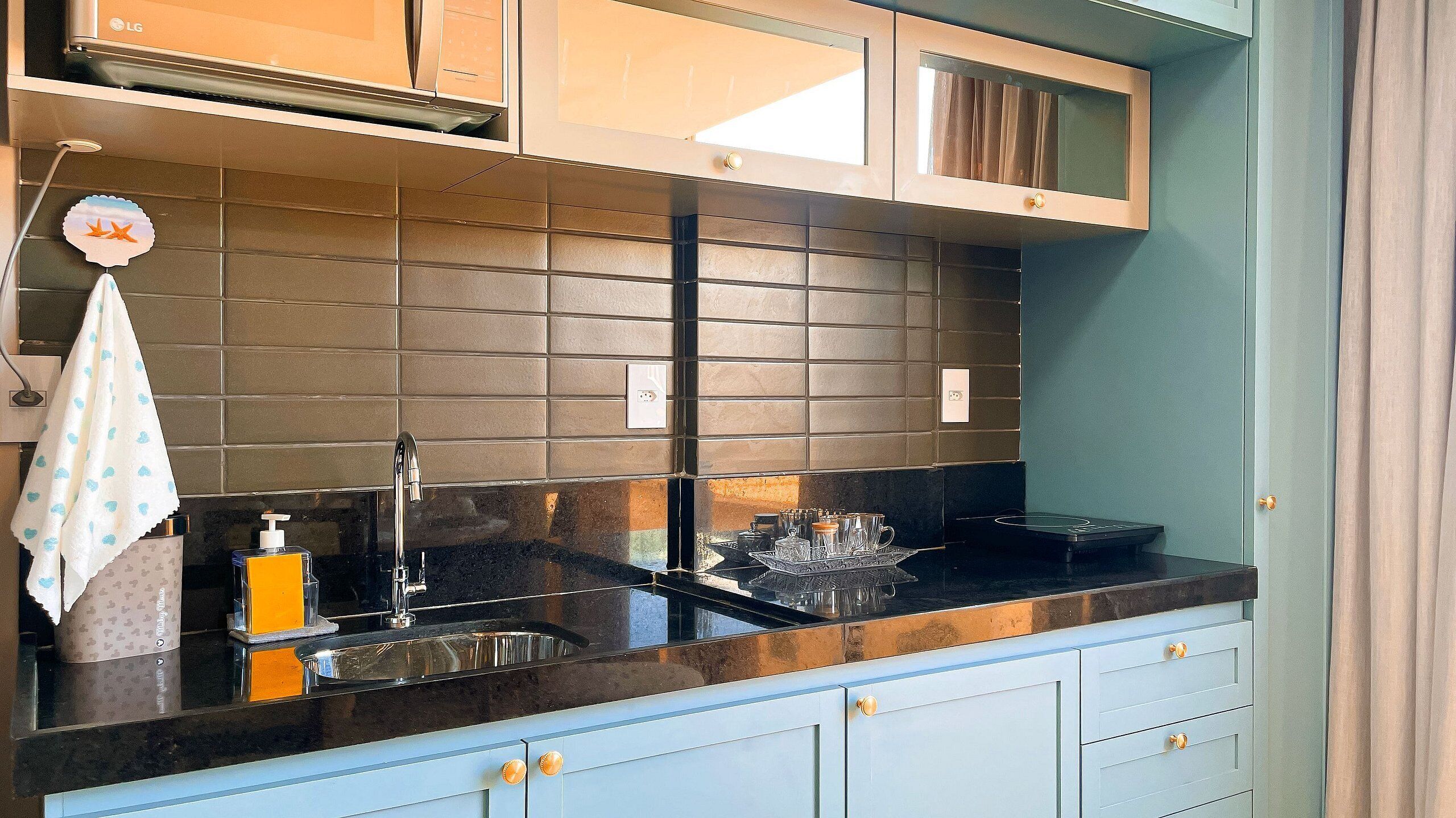 A kitchen with a black countertop, a stainless steel sink, and light blue cabinets.