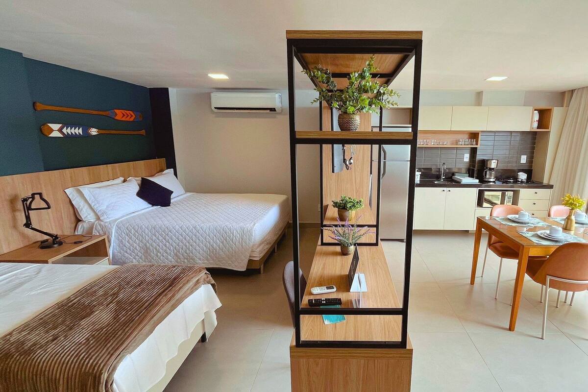 Une chambre d’hôtel moderne équipée d’un lit, d’une table de chevet, d’une lampe et offrant une vue sur la cuisine et l’espace repas.