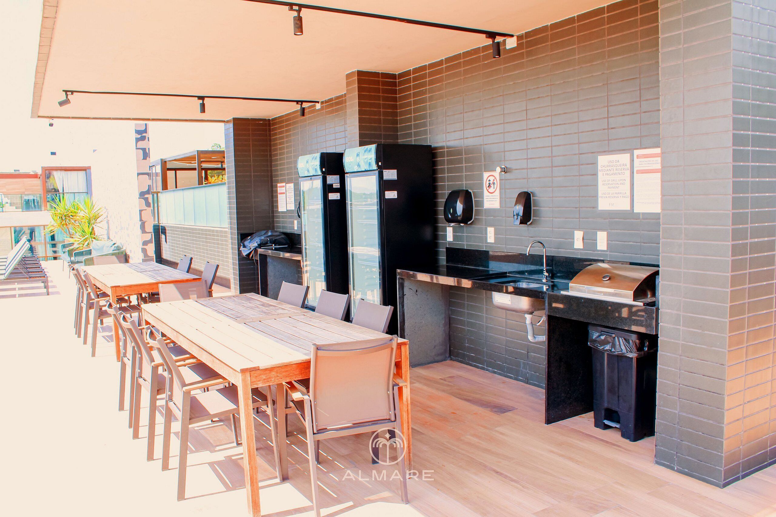 An outdoor dining area with a long wooden table and chairs, a grill station, and a trash bin.