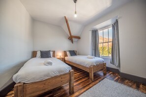 Un dormitorio con dos camas de madera, techo inclinado y ventana con cortinas.