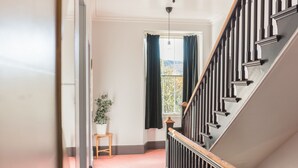 Eine Treppe mit Holzgeländer und Metallspindeln, die zu einem Raum mit rotem, gemustertem Teppich und einem Blumentopf führt.