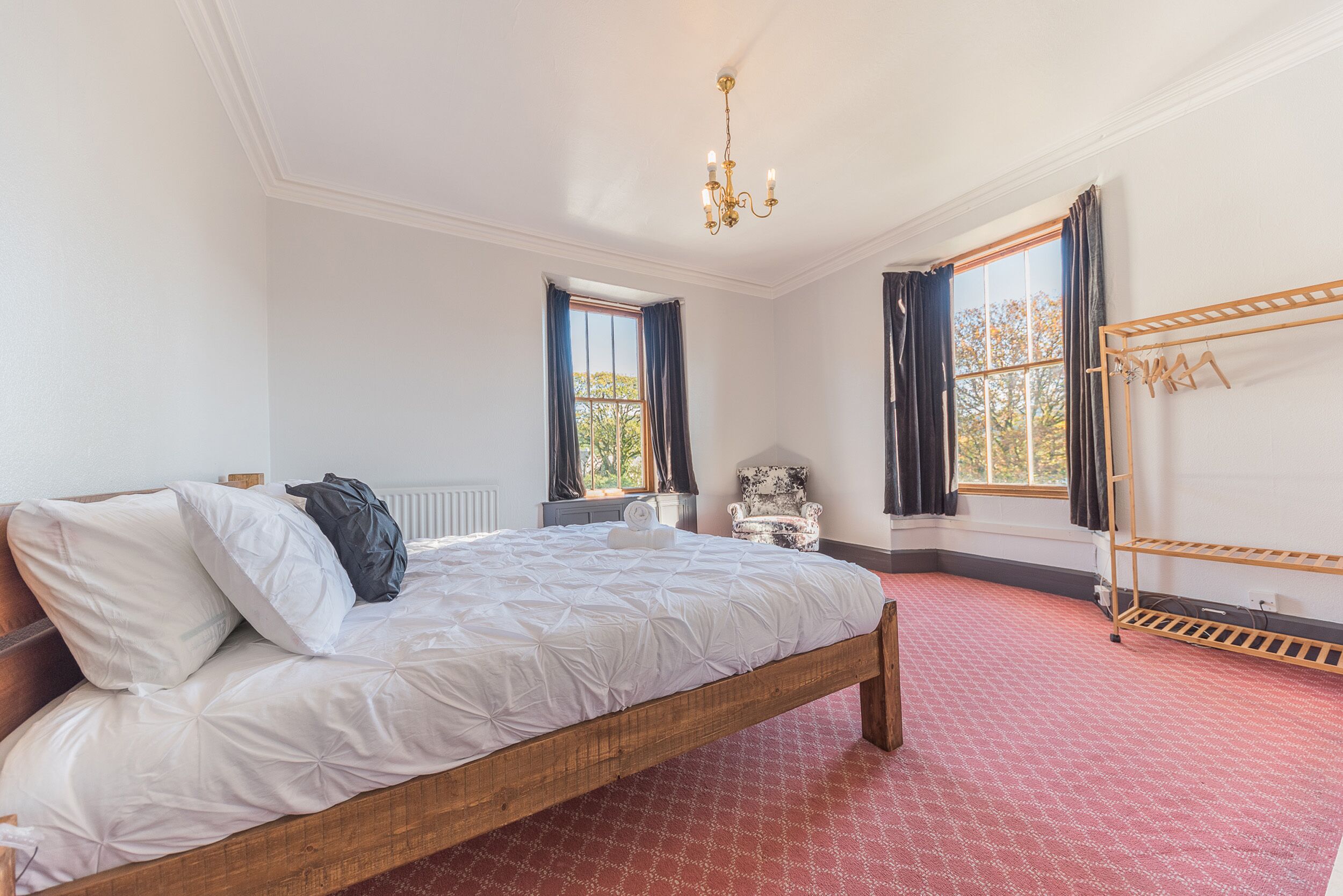Een slaapkamer met een houten bed, een radiator, een stoel en een raam met gordijnen.
