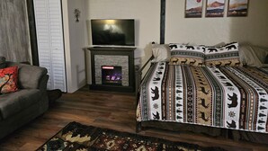Una habitación acogedora con chimenea, una cama con ropa de cama estampada, un sofá y un televisor.