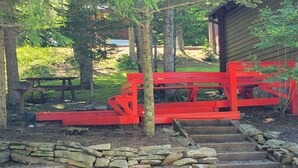 Un espacio al aire libre rústico con un banco de madera roja y escalones de piedra que llevan a una estructura de madera.