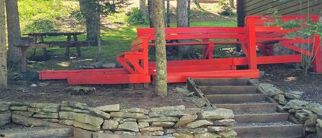 Un espacio al aire libre rústico con un banco de madera roja y escalones de piedra que llevan a una estructura de madera.