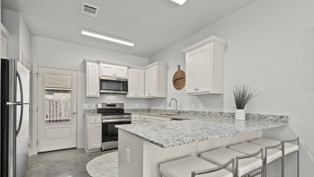 A modern kitchen with white cabinetry, a granite countertop, and a built-in island with bar stools.