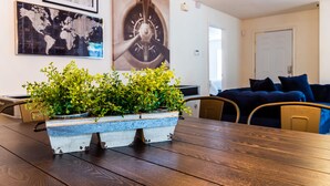 A dining table with a rustic blue planter with green plants, a world map, and a large clock on the wall.