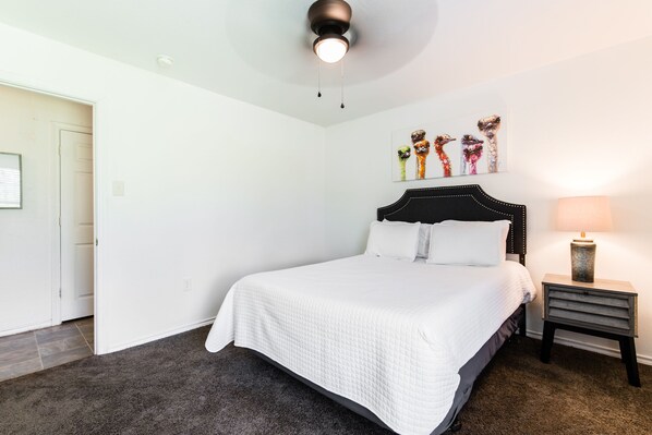 A neatly arranged bedroom with a large bed, a bedside table with a lamp, and a wall-mounted artwork of colorful animal heads. - Urban Chic - Perfect for Groups! (Dallas)