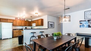 A modern kitchen with wooden cabinets, a white refrigerator, and a dining area with a dark wooden table and chairs.