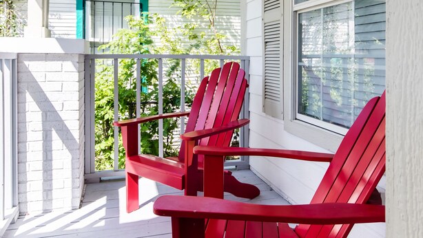 A porch with two red Adirondack chairs, a white railing, and a window with shutters.