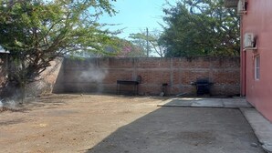 A backyard with a brick wall, two barbecue grills, and a small concrete patio.