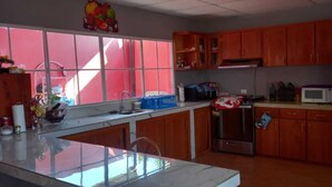 A kitchen with wooden cabinets, a stainless steel refrigerator, a microwave, and a window with a red view.