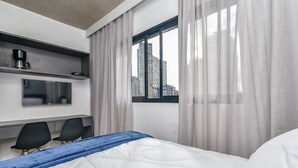 A hotel room with a bed, a desk with two chairs, a TV, and a window with curtains. - Vossa Bossa VN Ueno (São Paulo)