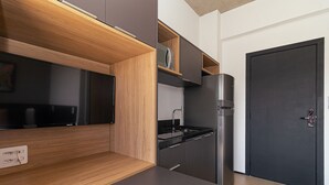 A modern kitchen with a built-in oven, a microwave, and a black refrigerator. There is a wooden countertop and a black cabinet. - Vossa Bossa VN Ueno (São Paulo)