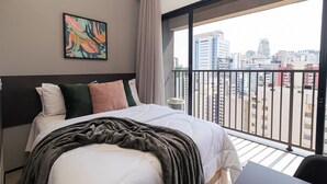 A modern hotel room with a large bed, a city view balcony, and a painting on the wall. - Vossa Bossa VN Ueno (São Paulo)
