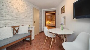 Una habitació amb paret de maó blanc, una banca de fusta amb coixins, una taula rodona amb cadires i un televisor de pantalla plana fixat a la paret.