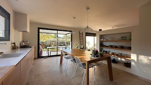Une cuisine moderne dotée d’une grande table à manger, de portes-fenêtres coulissantes donnant sur un patio et d’étagères intégrées pour ranger les ustensiles de cuisine.