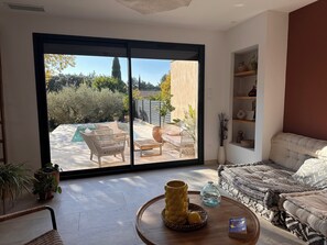 A spacious living room with a large sliding glass door leading to a patio with a pool, outdoor furniture, and a view of the surrounding garden. - Quiet villa with pool  (Sommières)