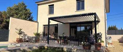 A modern two-story house with a covered patio, outdoor seating, and a swimming pool.