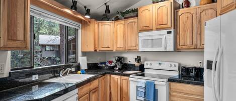 A modern kitchen with wooden cabinets, a white stove, a microwave, and a sink.
