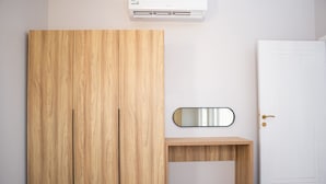 Een kamer met een houten garderobe, een klein houten bureau, een spiegel en een witte deur.