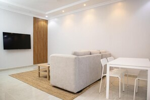 Een moderne woonkamer met een bank, een flatscreen televisie, een eettafel met stoelen en een houten accentmuur.