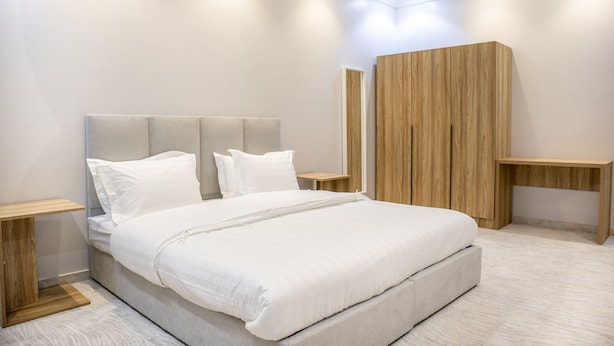 Een moderne slaapkamer met een groot bed, een houten hoofdbord, nachtkastjes en een houten garderobe.