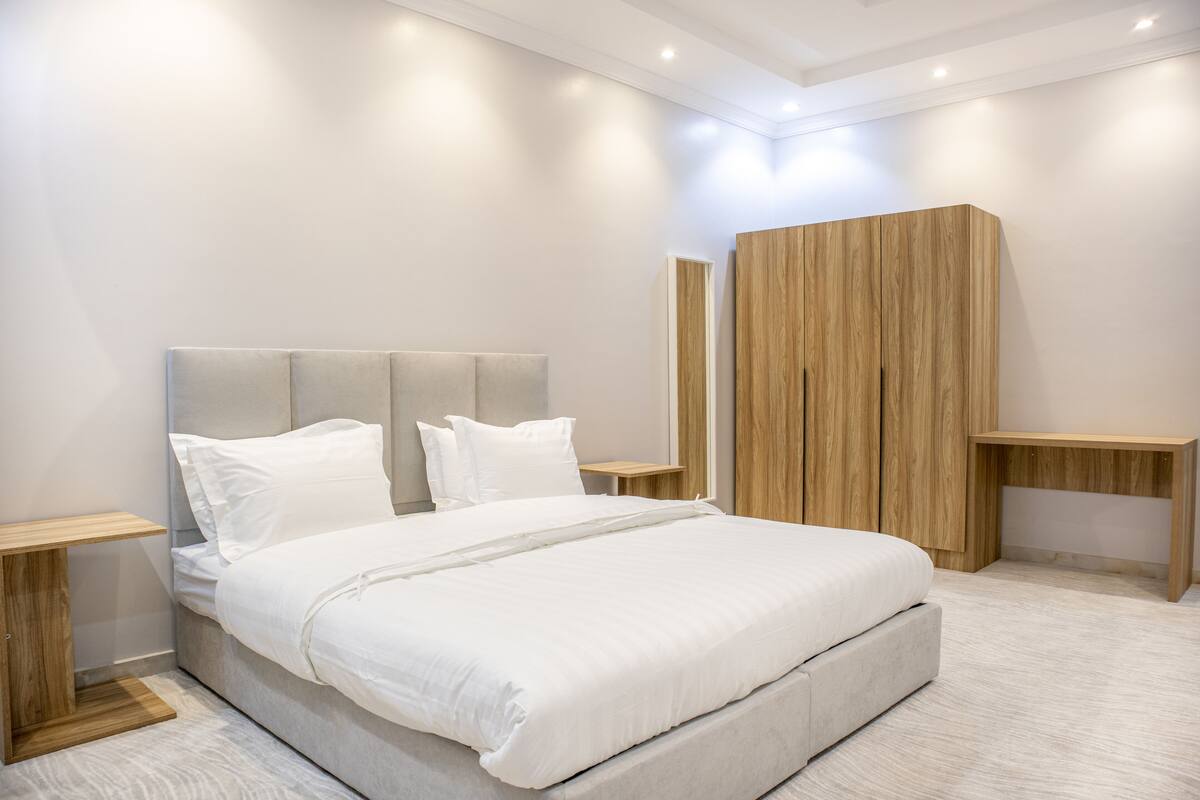 A modern bedroom with a large bed, wooden headboard, bedside tables, and a wooden wardrobe.
