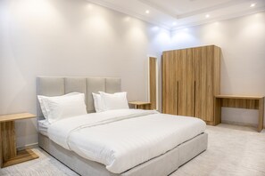 A modern bedroom with a large bed, wooden headboard, bedside tables, and a wooden wardrobe. - Family Apartments 15 Mins Drive to Al-Masjid Nabawi - Nozol Noor 4 (Madinah)
