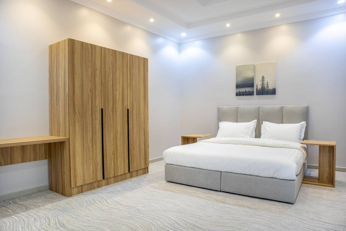 A bedroom with a bed, nightstands, a wooden wardrobe, and two wall-mounted paintings.