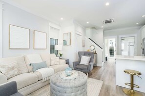 Un salon moderne comprenant un canapé, un fauteuil, un pouf et un tabouret de bar.