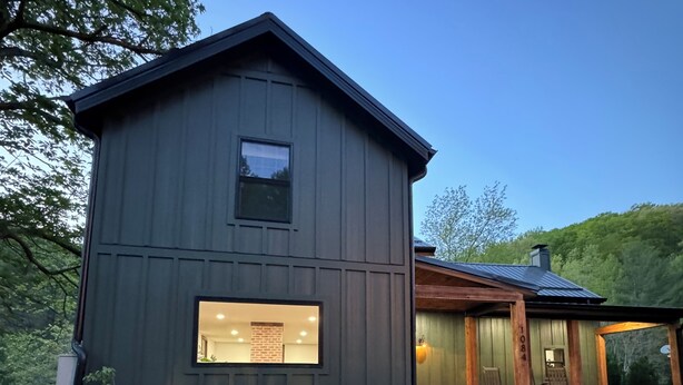 A modern two-story house with a dark exterior, a visible window with a plaque, and a well-maintained lawn with purple flowers. - Charming cozy RIVERFRONT cottage on the Piney River. A little slice of heaven! (Roseland)