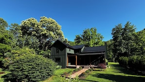 A modern house with a dark green exterior, a covered porch, and a well-maintained garden. - Charming cozy RIVERFRONT cottage on the Piney River. A little slice of heaven! (Roseland)