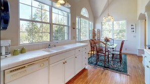 A kitchen with white cabinets, a large window, and a dining area with wooden chairs and a table.