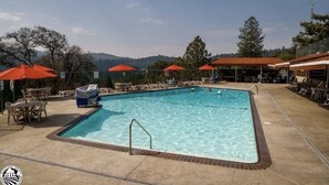 A rectangular pool with a metal ladder, surrounded by lounge chairs and orange umbrellas.