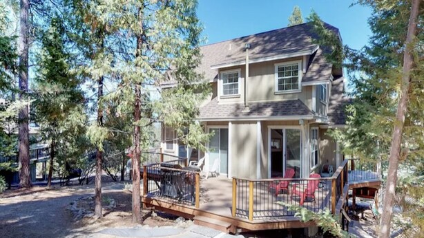 A two-story house with a deck, surrounded by trees.
