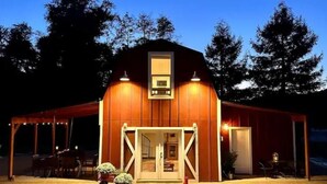 A wooden barn with a covered porch, a small entrance, and a dining area with tables and chairs. - Red Barn in Wine Country (Jacksonville)
