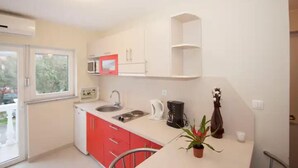 A compact kitchen with white and red cabinets, a microwave, a coffee maker, and a potted plant. - Two bedroom apartment for 4 person (Jadranovo)
