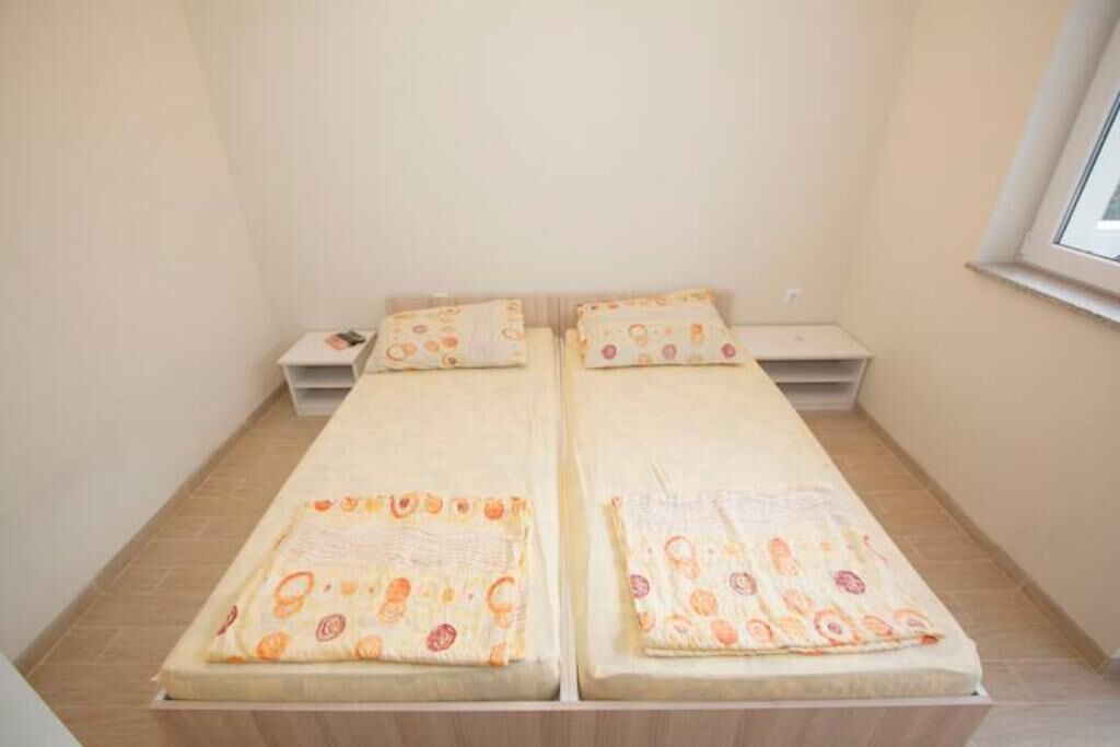 A small, single-room apartment with two beds, a small table, and a window.