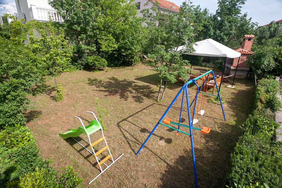 Een achtertuin met een schommel, een glijbaan en een klimrek.