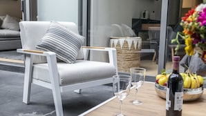 Un salón moderno con un sofá blanco, un cojín a rayas, una cesta tejida, una botella de vino y un cuenco con fruta sobre una mesa de madera.