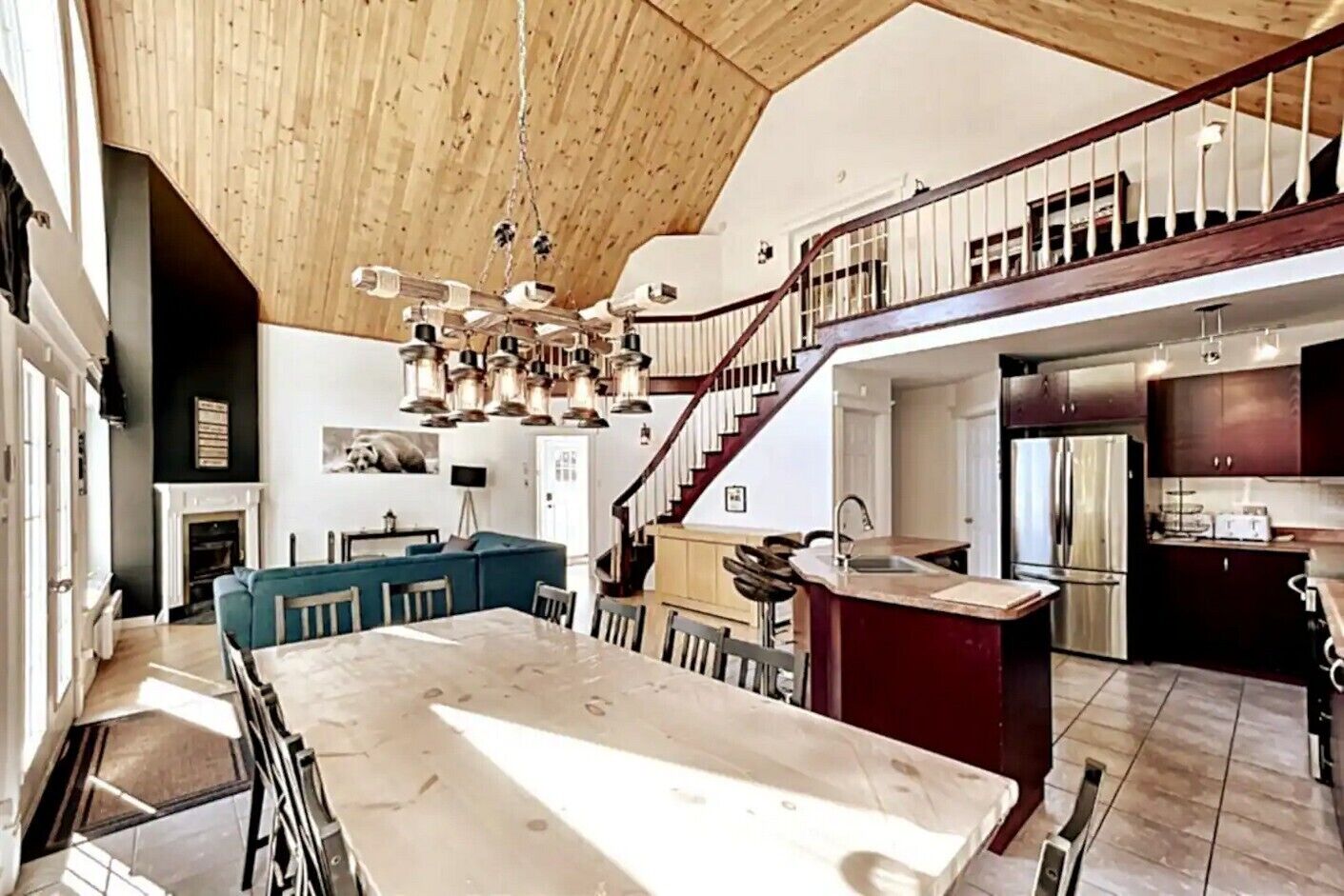 A spacious kitchen with a large island, a dining area with a marble table, and a staircase leading to an upper level.