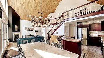 A spacious kitchen with a large island, a dining area with a marble table, and a staircase leading to an upper level.